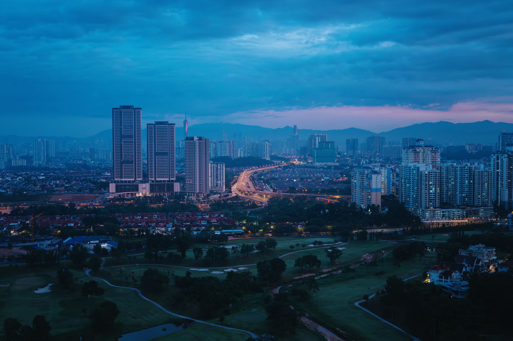 The Kuala Lumpur skyline at dusk, with a lit highway curving through the city